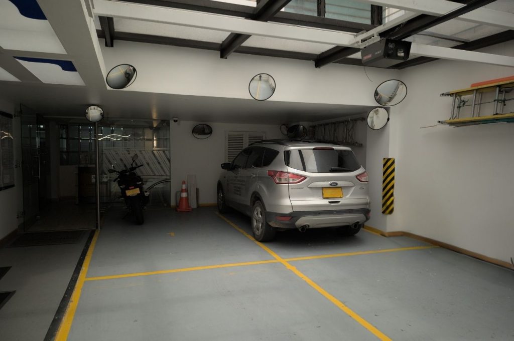 Amplio parqueadero subterráneo en Coworking Marbella con cámaras de seguridad y espejos para maniobras, ofreciendo comodidad y seguridad para vehículos de coworkers y visitantes en Bogotá.