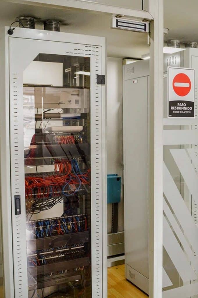 Rack de servidores con cableado organizado y señal de "Paso Restringido", indicando la robusta infraestructura tecnológica y seguridad en Coworking Marbella en Bogotá.