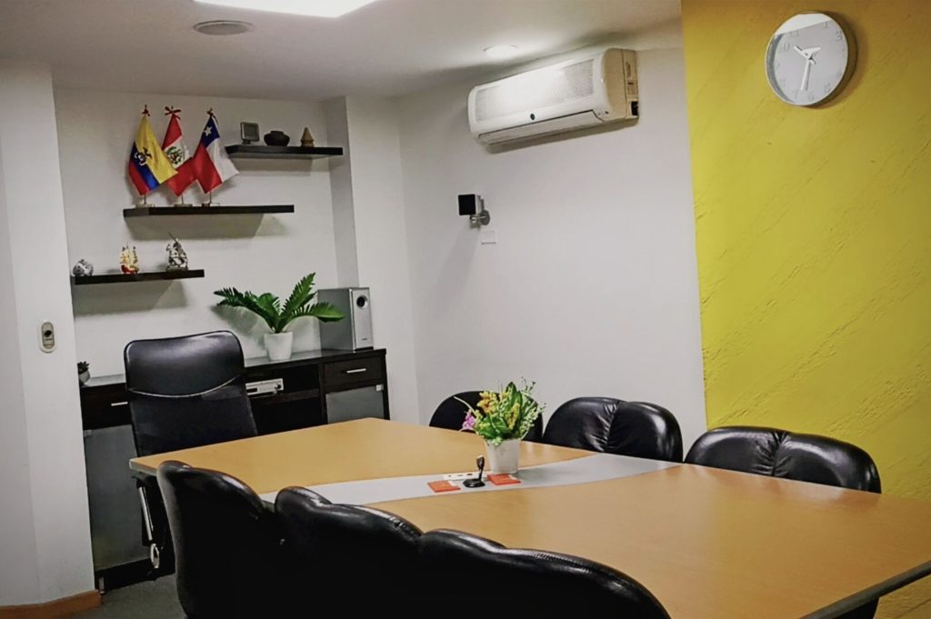 Sala de reuniones profesional en Coworking Marbella con mesa de juntas, sillas cómodas, banderas decorativas y aire acondicionado, ideal para encuentros corporativos en Bogotá.