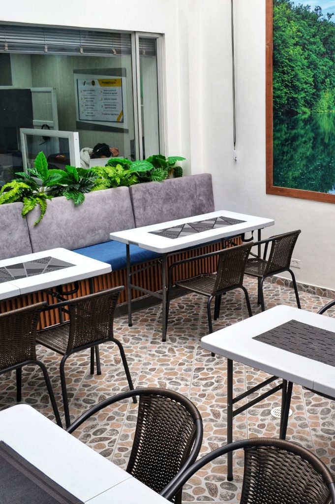 Área de comedor o descanso informal en Coworking Marbella con mesas y sillas, decorada con un cuadro de paisaje natural, ideal para pausas y socialización.
